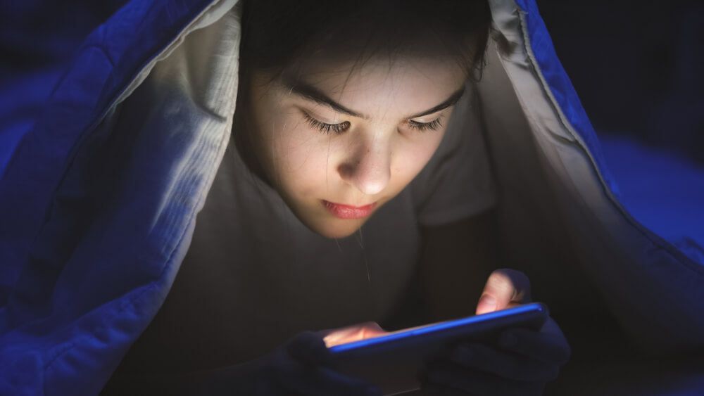 ragazzina usa smartphone al buio sotto le coperte