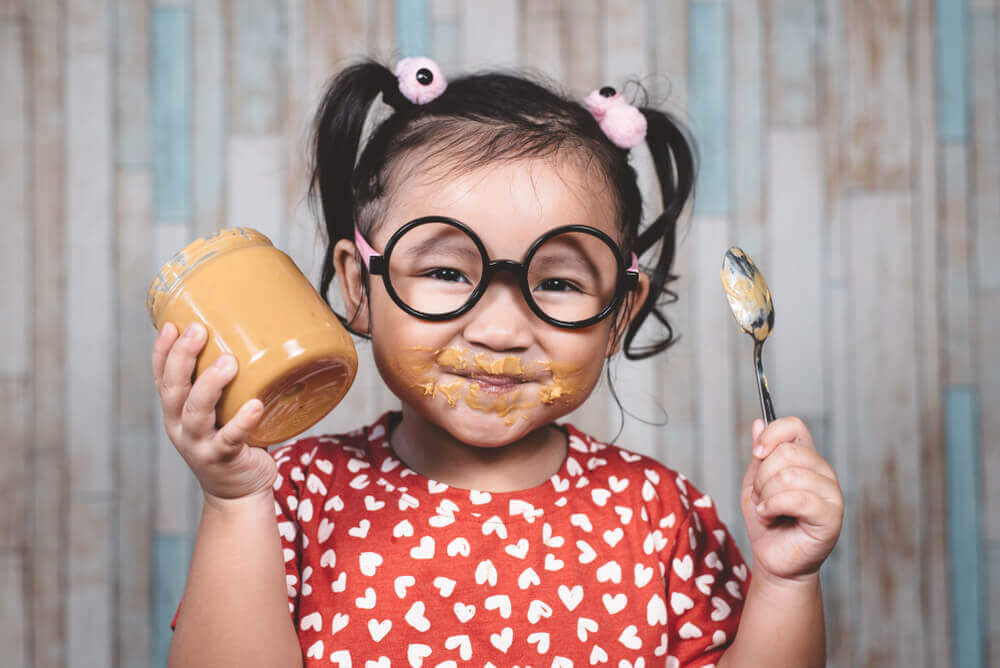 bambina felice mangia burro d'arachidi liscio per prevenire allergia