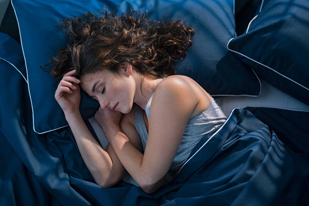 donna dorme con cuscino sotto la testa sulle lenzuola blu con capelli sciolti