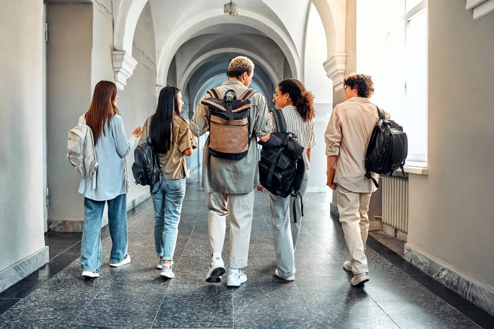 studenti camminano di spalle in università con zaino sulle spalle