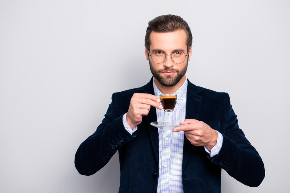 uomo con giacca cravatta e occhiali da vista beve caffè al vetro in tazza trasparente