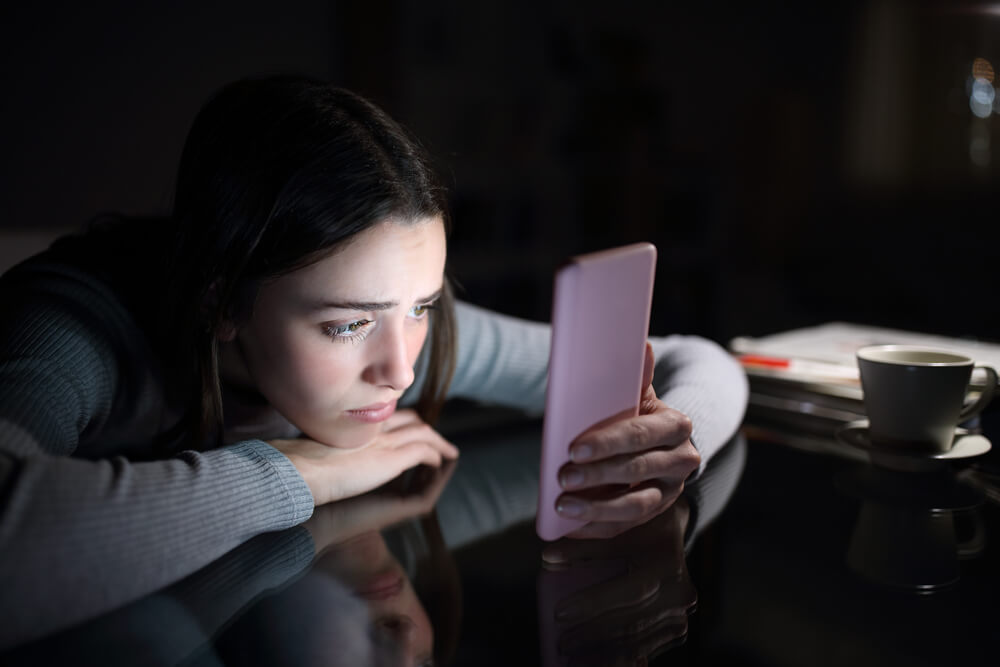 ragazza usa smartphone al buio. la sovraesposizione ai social media è uno dei fattori alla base del fenomeno dell'hikikomori