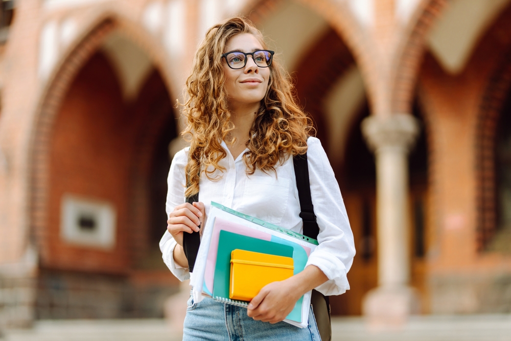 studentessa università con occhiali neri camicia bianca capelli lunghi rossi e libri in mano