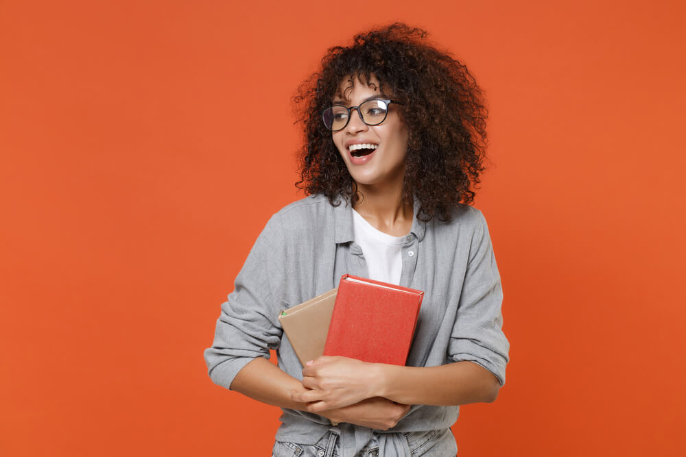 ragazza riccia con occhiali da visata stringe libri al petto