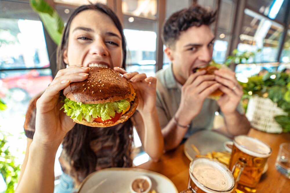 un ragazzo e una ragazza mangiano hamburger cibo spazzatura in un fast food