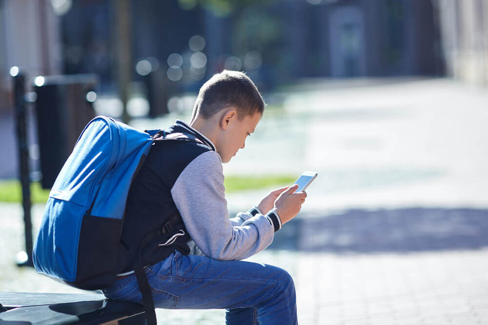 bambino usa smartphone con zaino in spalla per rappresentare divieto smartphone a scuola