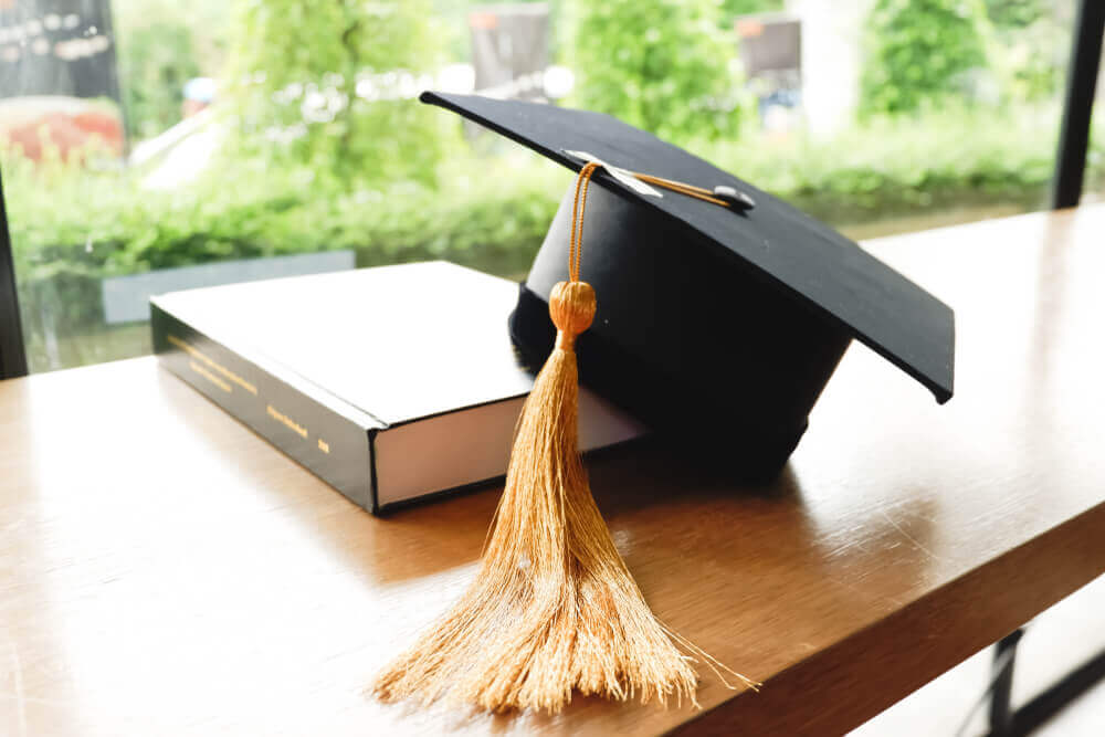 tocco di laurea appoggiato su libro per rappresentare come scegliere l'argomento della tesi