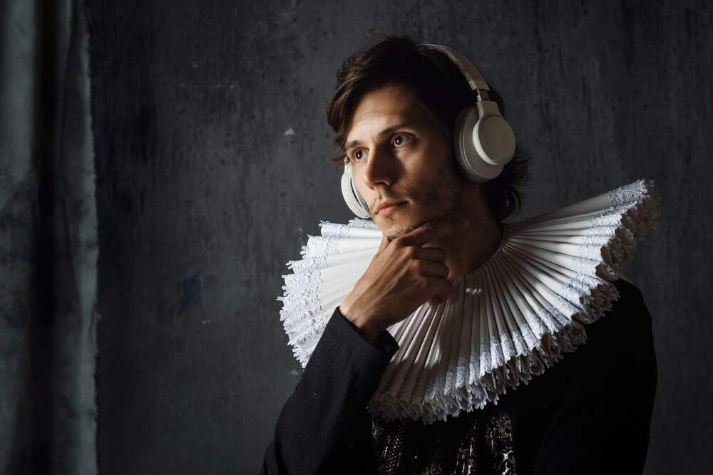 Giovane uomo con collare medievale ascolta musica o podcast con cuffie alle orecchie