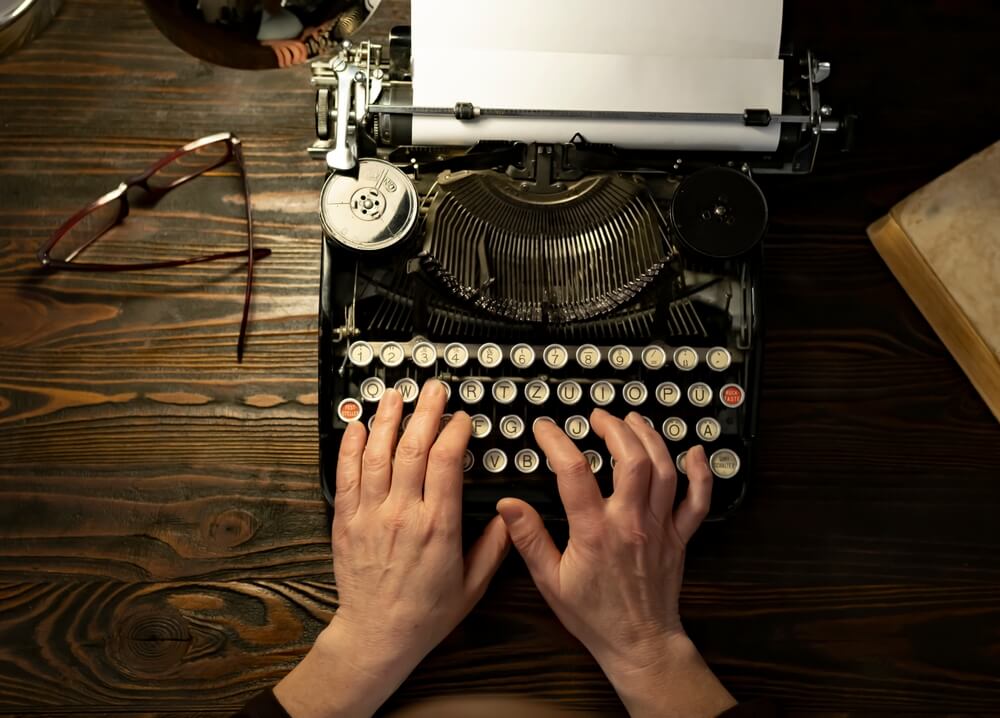 Focus su mani di scrittore che scrivono a una macchina da scrivere vintage