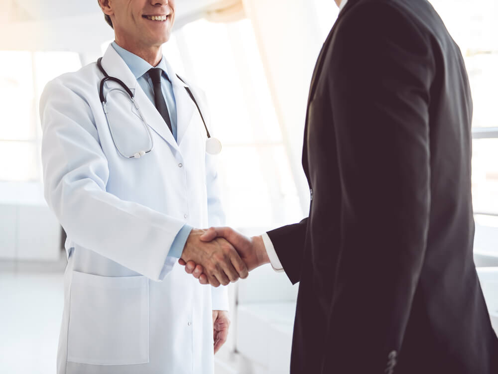 medico maturo e giovane uomo d'affari si stringono la mano mentre si trovano nella sala di un ospedale