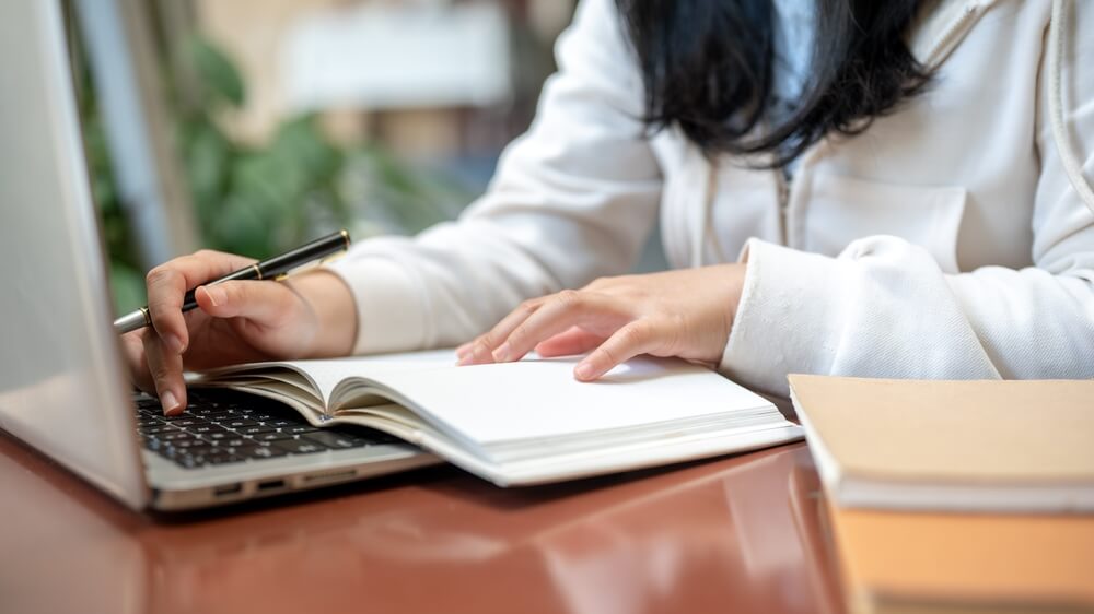 A,Cropped,Image,Of,An,Asian,Female,College,Student,Is Ragazza scrive su un libro di testo