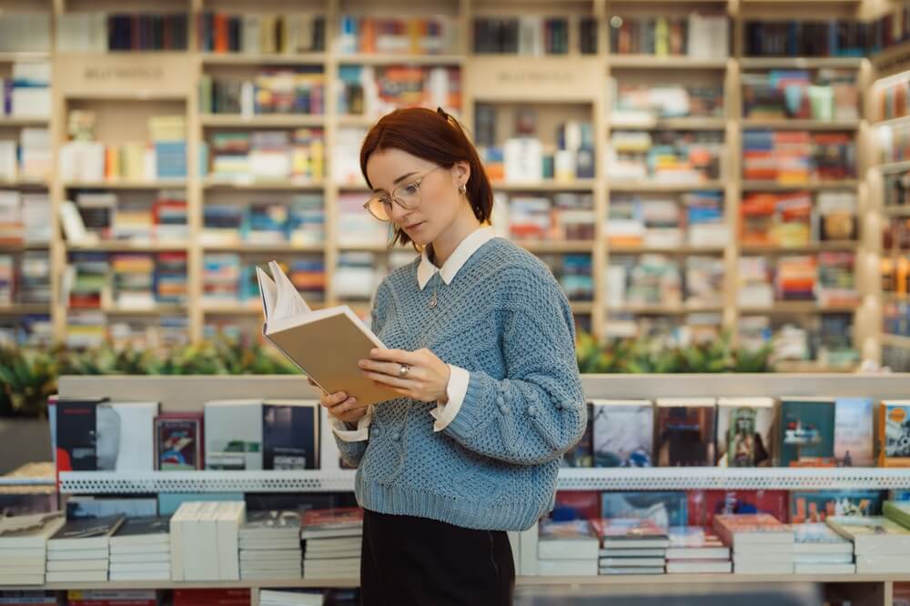 Ragazza con occhiali legge un libro in piedi in libreria