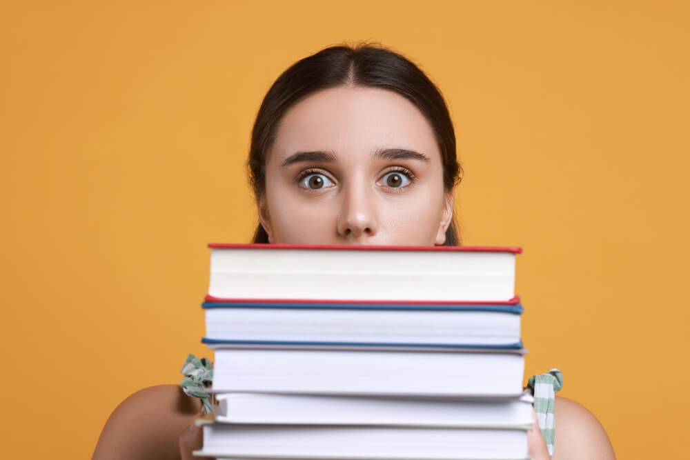 Studentessa stressata con pila di libri davanti al viso