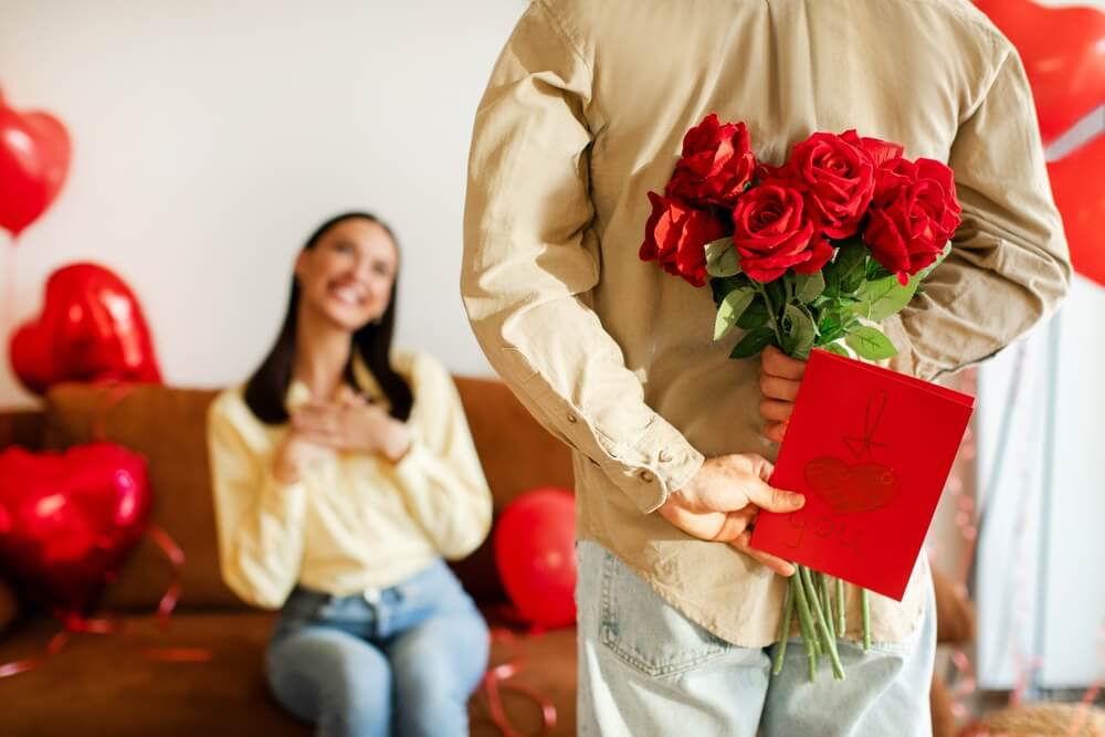 Uomo nascone mazzo di rose e biglietto d'amore dietro la schiena per fare una sorpresa alla sua fidanzata, che è davanti a lui
