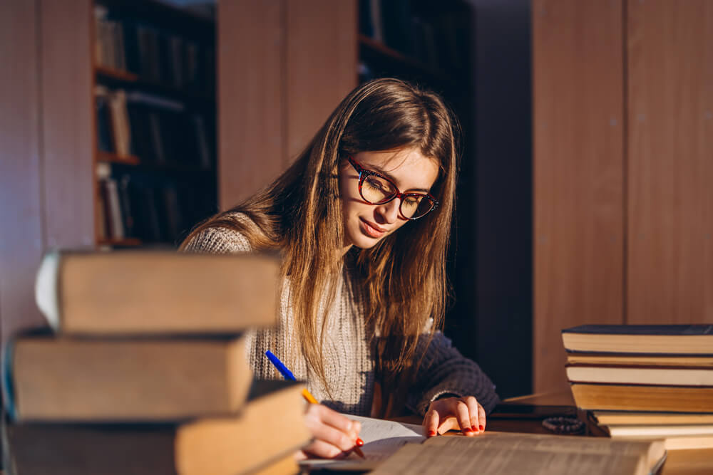 Studentessa in biblioteca studia con una pila di libri sulla scrivania