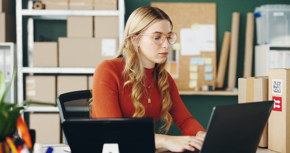 Woman,,Computer,And,Logistics,With,Boxes,For,E,Commerce,,Package Ragazza e-commerce manager al pc con scatole di cartone sullo sfondo