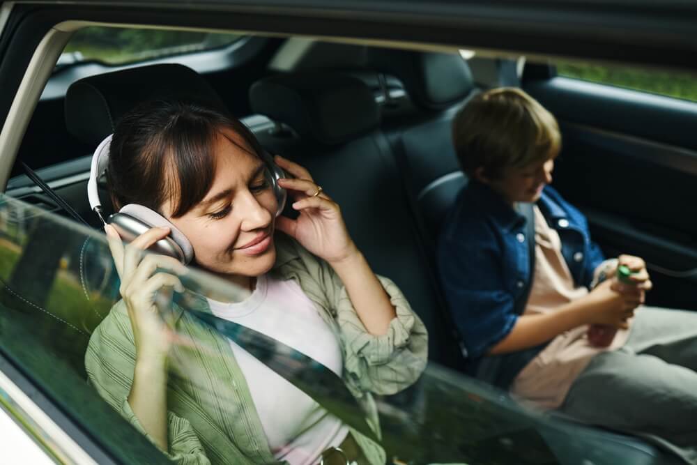 Caucasian,Young,Adult,Woman,Sitting,In,Car,Listening,To,Music Donna ascolta la musica in cuffia durante un viaggio di famiglia in macchina