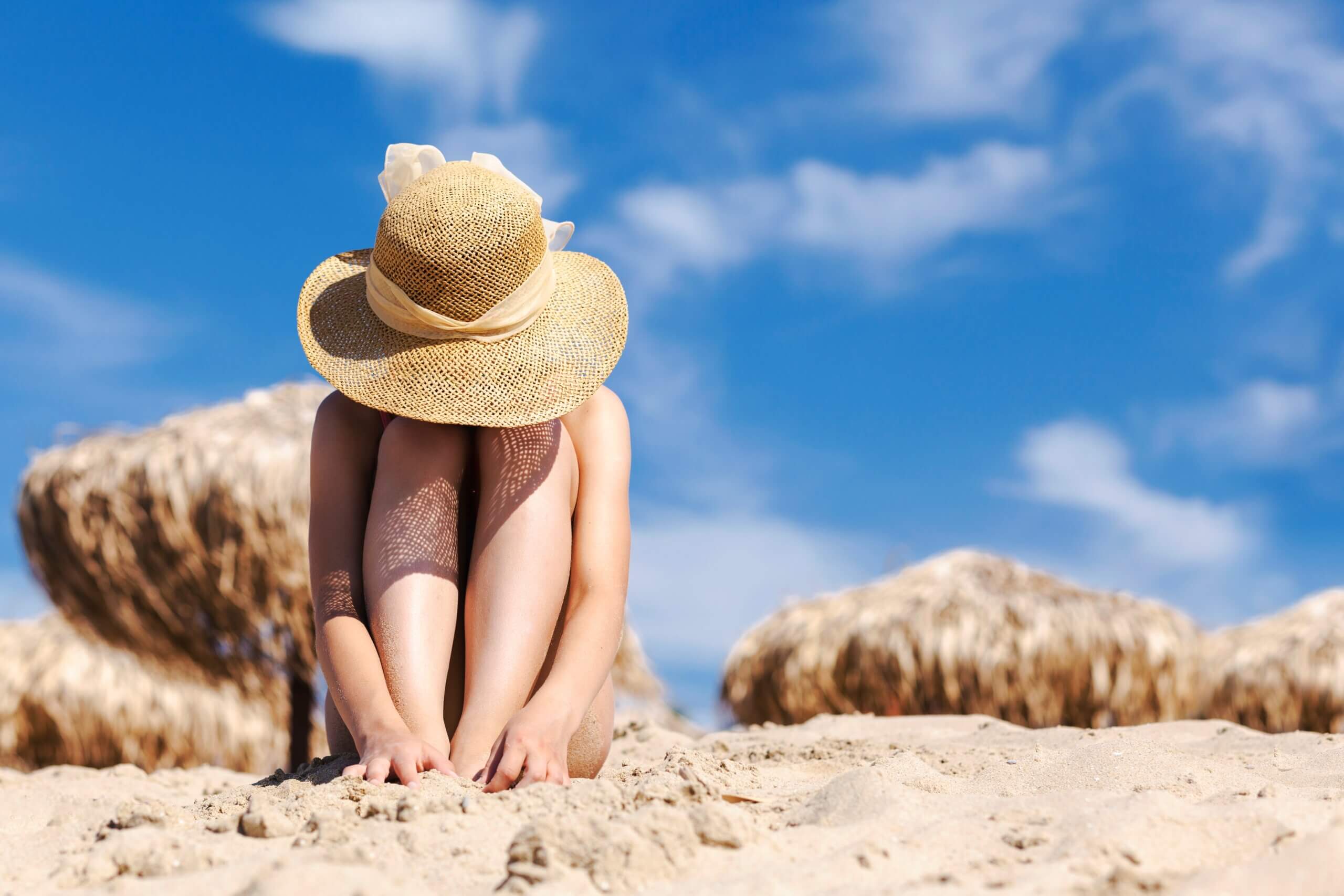 Ragazza depressa in riva al mare si copre il viso col cappello di paglia