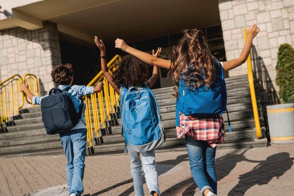 shutterstock_2490871645 bambini delle elementari felici entrano a scuola durante piano estate 2026