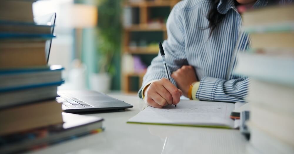 Studentessa universitaria china sulla scrivania con davanti due pile di libri