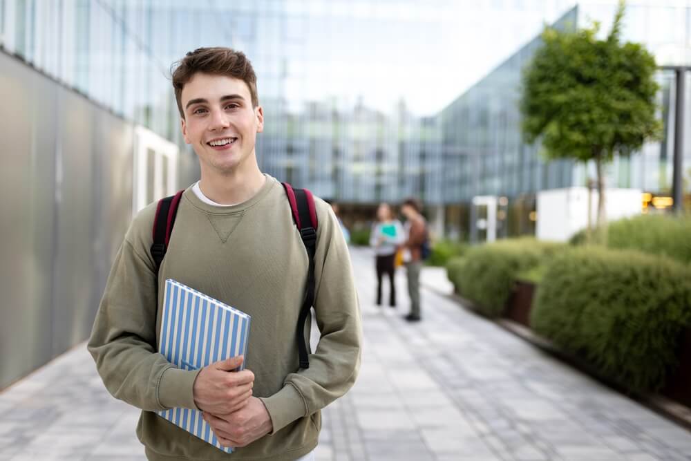 Studente universitario che tiene il libro di testo fuori dall'edificio universitario
