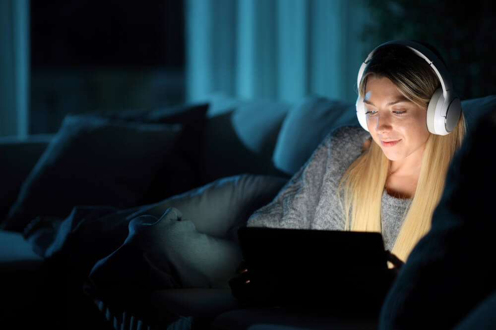 Donna con le cuffie che guarda film sul tablet di notte seduta su un divano a casa
