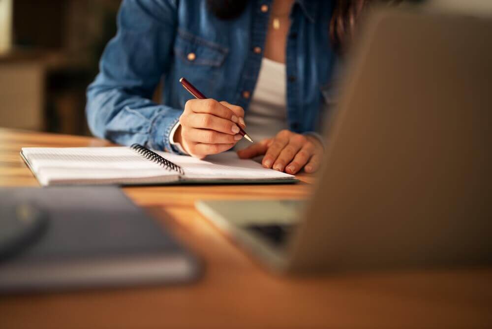 studente di ateneo online studia con quaderno e laptop alla scrivania per rappresentare l'aumento degli iscritti alle università telematiche
