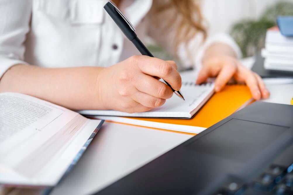 Primo piano di donna che scrive su un block notes.