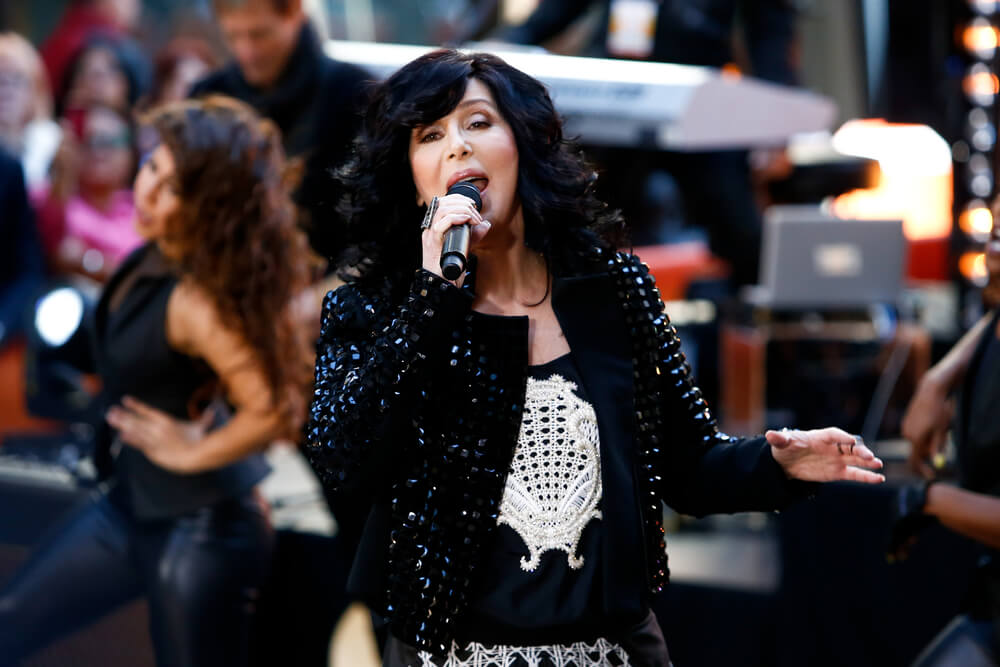 Cher canta tra la folla con microfono in mano e una giacca nera