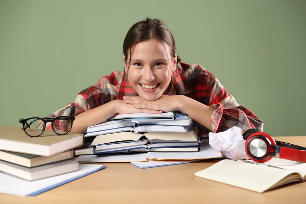 Ritratto di studentessa che sorride mentre prepara gli esami e posa su una pila di libri