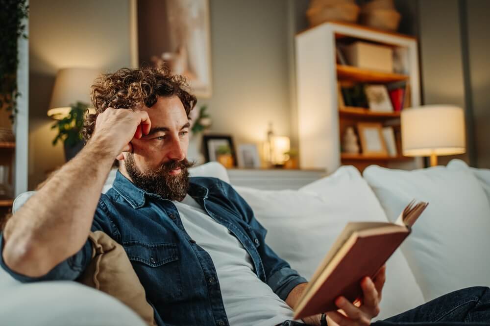 Uomo con barba e baffi sul divano legge un libro