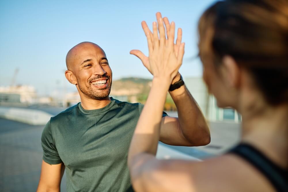Smiling,Active,Young,Couple,Jogging,Exercising,And,Having,Fun,And Allenatore sportivo e atleta si scambiano un gesto di intesa sorridendo