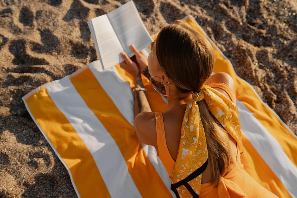 Ragazza con costume giallo legge libro su telo mare in spiaggia