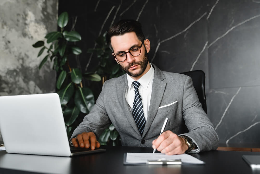 Focused,Young,Businessman,Signing,Up,The,Documents,Of,Employment,While legal specialist a lavoro prende appunti con un laptop davanti