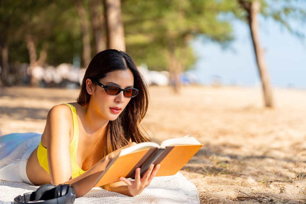 ragazza legge libro in spiaggia con occhiali da sole