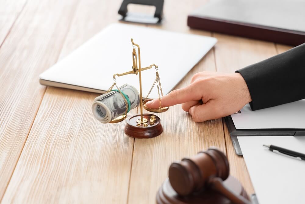 Hand,Balancing,Money,And,Justice,Scales,With,A,Gavel,On Mano che bilancia denaro e giustizia con un martelletto su una scrivania di legno, finanza legale e corruzione